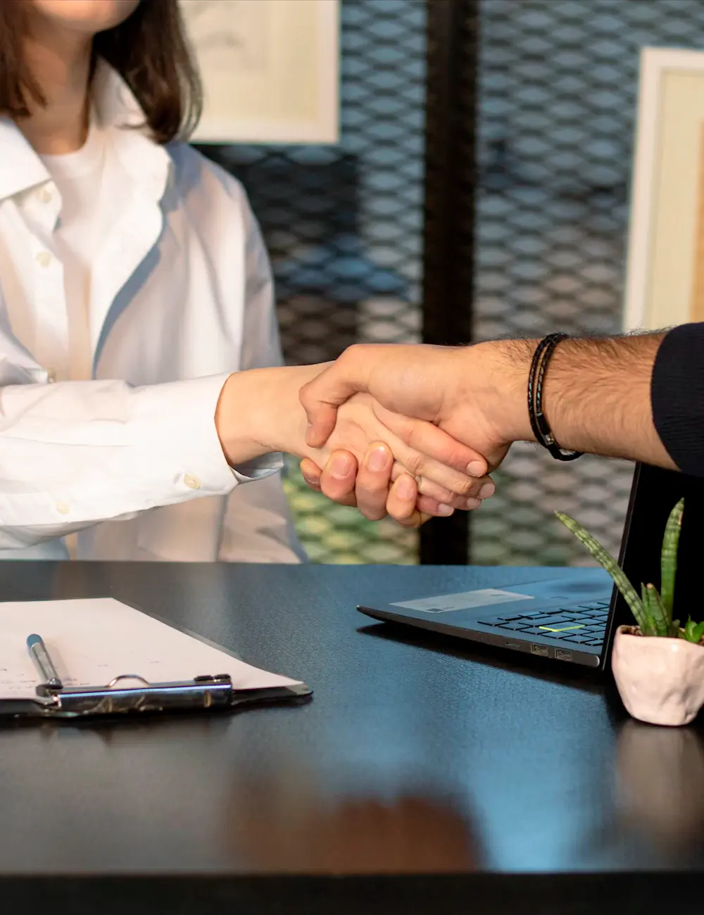 Dos personas cerrando un acuerdo con un apretón de manos sobre una mesa